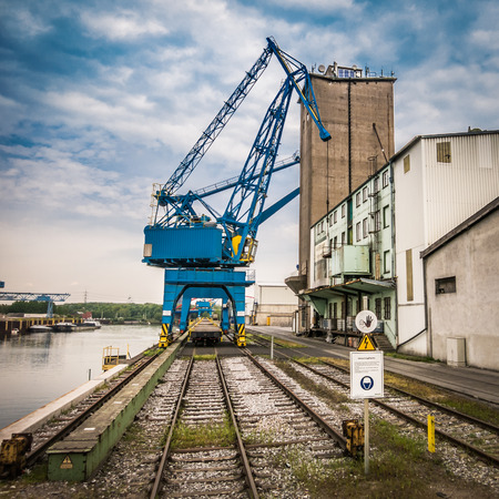 A blue harbor crane in a inland port in Germany, a few warehouses, rails and a blue sky with a few clouds の写真素材