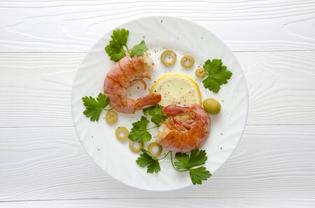 grilled two large shrimp on a round white plate on a white wooden background with lemon parsley and spices top viewの写真素材
