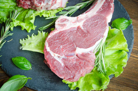 raw entrecote black plate wooden table with rosemary and herbs selective focusの写真素材