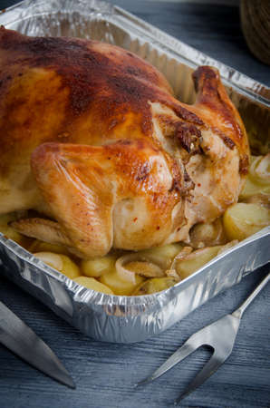 baked chicken carcass knife fork baking foil with potatoes on a gray wooden backgroundの写真素材