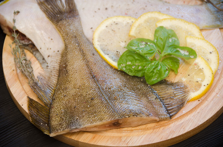 Raw fish sole round cutting board basil on a black wooden background close upの写真素材