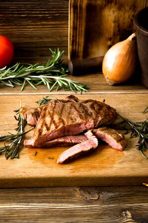 rare steak rosemary rectangular wooden cutting board spices on a brown wooden backgroundの写真素材