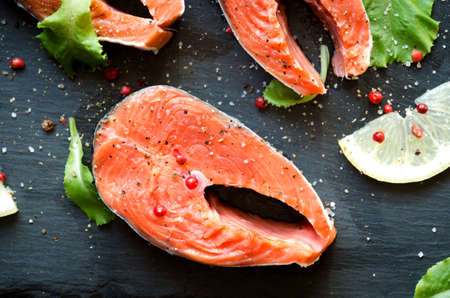 Salmon steaks salt greens black square plate lemon on dark background close-upの写真素材