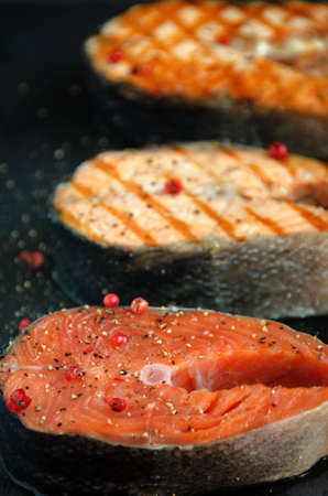 group salmon steaks pepper dark square plate on dark background close-upの写真素材
