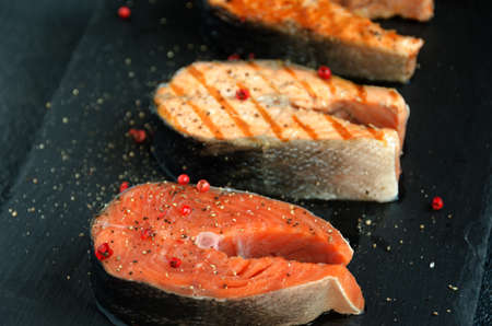 three salmon steaks pepper black square plate on dark background close-upの写真素材