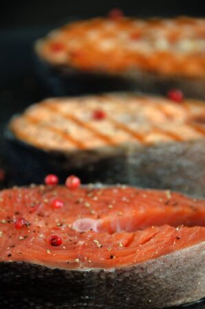three salmon steaks pepper dark square plate on dark background close-upの写真素材