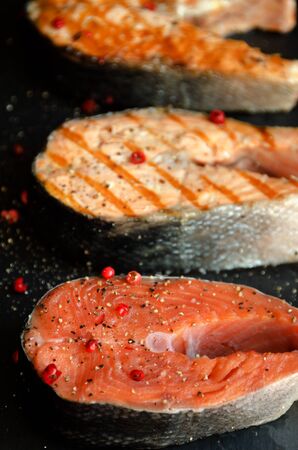 Several salmon steaks pepper black square plate on dark background close-upの写真素材
