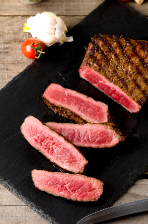 black angus rare steak sliced dark plate on a gray wooden backgroundの写真素材