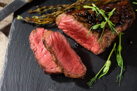 sliced rare steak black angus top view on black rectangular plate with pea sprout thyme rosemary spiceの写真素材