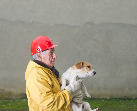 Old man in safety suit holds dog in his armsの写真素材