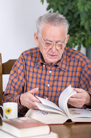 Old man with reading glasses looking for something in old bookの写真素材