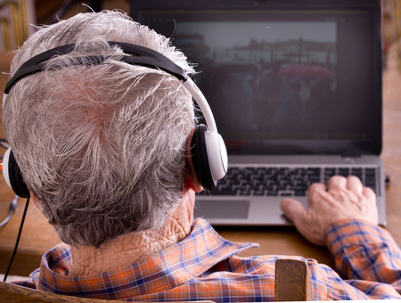 Old man with headset looking at laptop