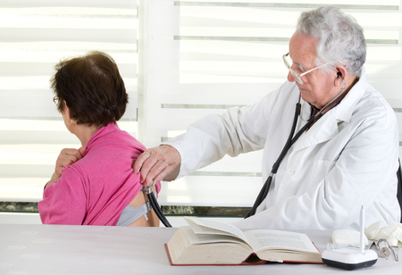 Senior doctor listening patient's heartbeat with stethoscopeの写真素材