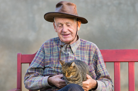Old man with hat sitting with cat in his lapの写真素材