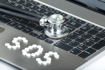 SOS sign written with white pills and stethoscope on keyboard of laptopの写真素材