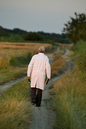 Tired old agronomist in white coat leaving field after hard workの写真素材