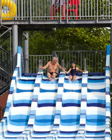 Young girl with grandpa sliding on toboggan in water park
