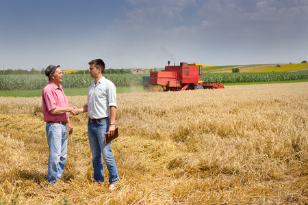 Peasant and businessman shaking hands on wheat field