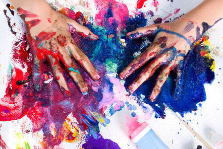 Painted hands smudging colors on messy paperの写真素材