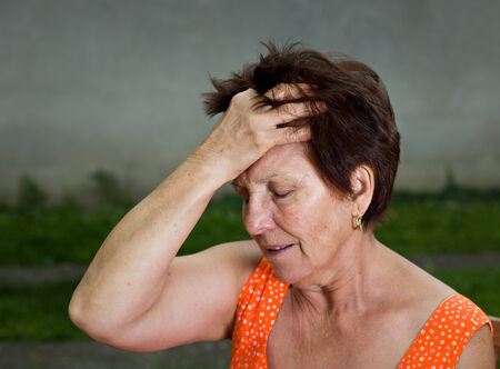 Senior woman suffers from headache, holding hand on head and have pain faceの写真素材