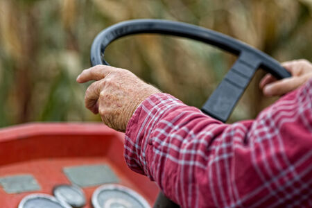 Close up of old male hands on steering wheel driving tractorの写真素材