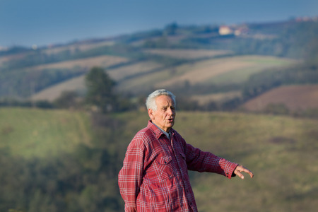Senior man in plaid shirt walking in nature, hills in backgroundの写真素材