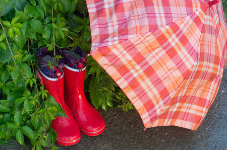 Red girlish gumboots and open umbrella drying in gardenの写真素材
