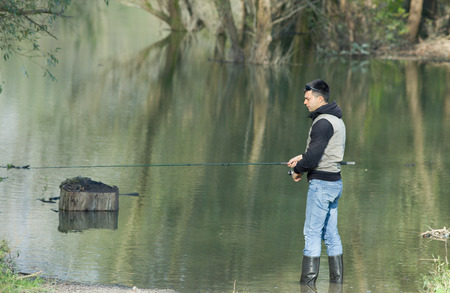 Young man fishing on small river in autumn time