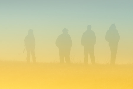Silhouettes of small group of people walking on meadow on foggy morningの写真素材