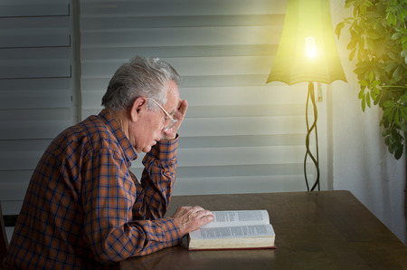 Senior man sitting at dining table and reading a book
