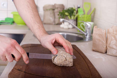 Close up of male hands slicing raw wholemeal bread on kitchen countertopの写真素材