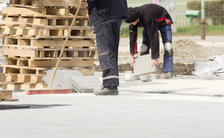 Construction worker in safety clothes cleaning building site after installing flagstones in sandの写真素材