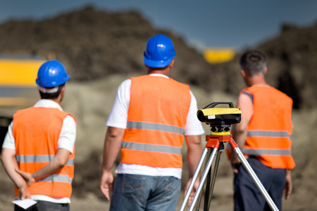 Theodolite on tripod at road construction site with workers supervising works