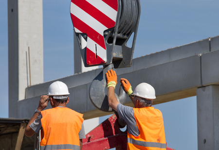 Construction worker navigating with concrete slab lifted by crane at building site