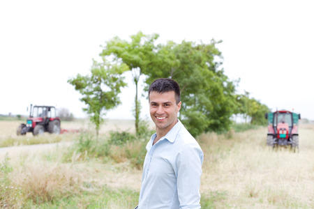 Young businessman standing in the field with two tractors in backgroundの写真素材