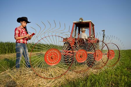Young girl farmer standing beside haying rake attached to tractor