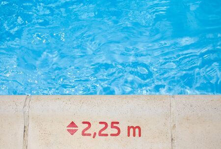 Swimming pool edge with warning sign about water depthの写真素材