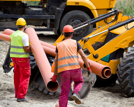Construction workers in safety cloths carrying pipes and loading bulldozer for transportation at building siteの写真素材
