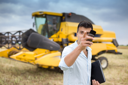 Young businessman holding cell phone in raised hand and talking to someone in rapeseed field....