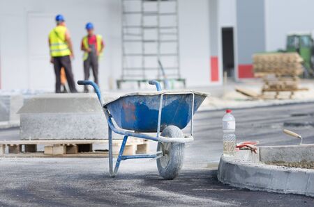 Dirty wheelbarrow standing at construction site, workers in backgroundの写真素材