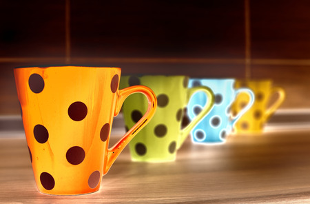 Close up of orange tea pot on kitchen countertop. Other colorful cups in backgroundの写真素材
