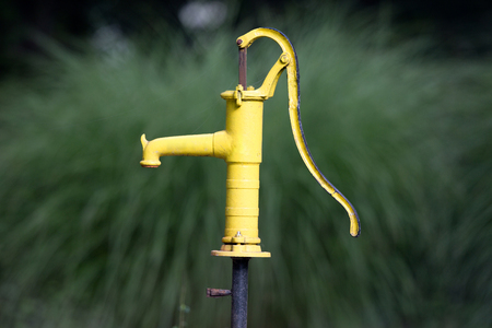 Yellow old water pumping well in courtyard with green backgroundの写真素材