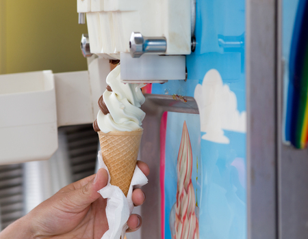 Human hand holding cone with swirled ice cream from machineの写真素材