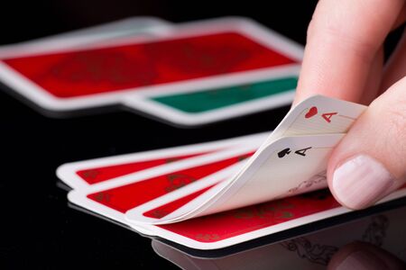 Human hand holding two aces in poker game, cards in background