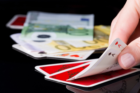 Human hand holding two aces in poker game, cards and money in background