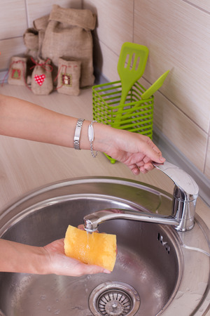 Close up of female hand holding sponge for dish washing under tap waterの写真素材