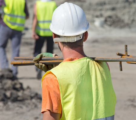 Construction worker carrying reinforcement rods on the shoulder. Rear view of man
