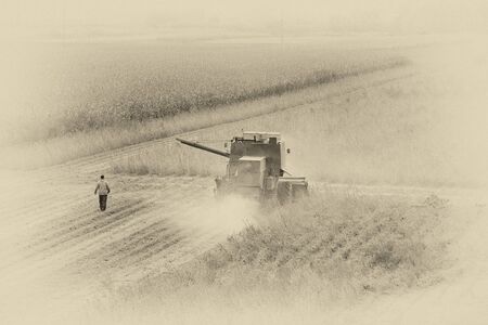 Old faded image of combine harvester working in fieldの写真素材
