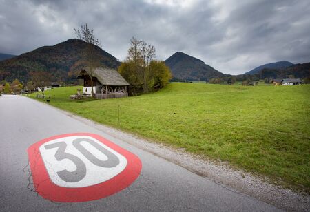Warning painted road sign of speed limit on the village entrance in mountain landscape