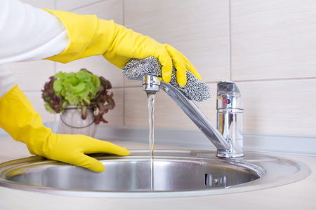 Close up of female hands with protective gloves scrubbing and cleaning kitchen faucetの写真素材